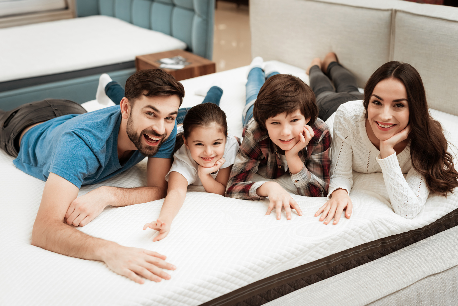 Happy family is relaxing on mattress in orthopedic furniture store. Big family check softness of mattress